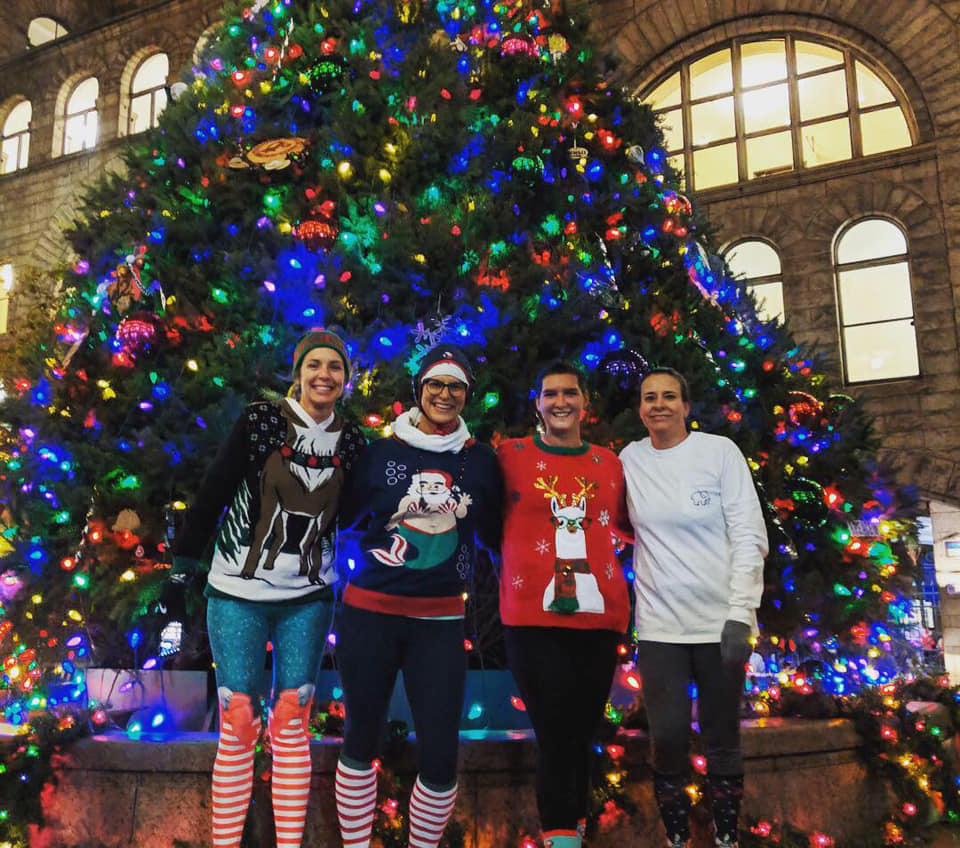 4 women water polo players in holiday sweaters in Pittsburgh in front of Christmas tree
